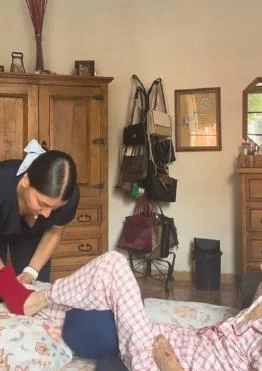 Una cuidadora acompaña a una persona mayor en una actividad en casa.
